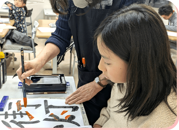 書道の筆使いを学ぶ女の子と先生