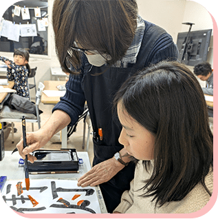 書道の筆使いを学ぶ女の子と先生