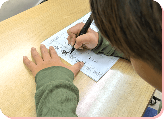 机に向かって文字を書く子どもの手元